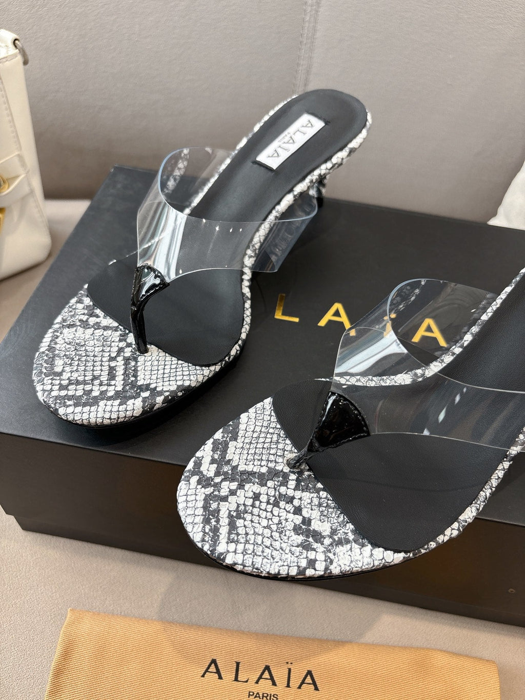 ALAIA HEELED THONG 25S 55 MM IN WHITE AND BLACK LAMBSKIN SNAKE-EMBOSSED WITH CLEAR STRAP